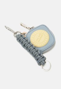 Pochette à pièces en tissu bleu avec un patch rond jaune portant la mention "You are enough,", attachée à un porte-clés tressé bleu et gris avec des anneaux métalliques.
