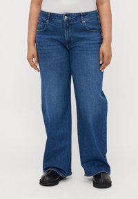 Baggy blue denim jeans with a high waist, featuring five pockets, a button closure, and a smooth texture. Straight-leg cut.