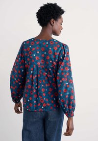 Kwiatowa bluzka w granatowym kolorze z czerwonymi i białymi wzorami kwiatów. Posiada długie, bufiaste rękawy i okrągły dekolt. Miękka tekstura materiału.