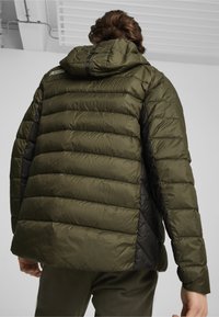 Puffers jakke i mørke olivengrøn med quiltet tekstur, sorte sidestykker og en hætte. Har et logo på ryggen nær halsudskæringen.