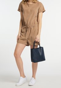 Hnědý semišový overal s krátkými rukávy a šňůrkou v pase, doplněný námořnickou perforovanou koženou taškou a bílými teniskami.