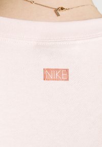 Světle růžové bavlněné tričko s žebrovaným výstřihem a malou tkanou nášivkou Nike v kontrastní broskvové barvě na zadní straně.