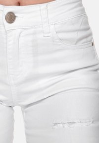 Jeans de mezclilla blanca con una cintura alta, bolsillos frontales y un detalle de rasgadura en el muslo izquierdo. Textura suave y mínima ferretería.