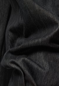 Nahaufnahme von zerknittertem schwarzem Nadelstreifenstoff mit detaillierter Textur und diagonaler Webmusterung.