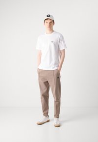 White short-sleeve t-shirt with small text detail, paired with beige tapered trousers featuring an accent logo, and white sneakers with gum soles.