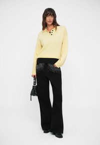 Yellow knit pullover with a collar and three buttons, paired with black flared pants featuring embellished pockets, and a small handbag.