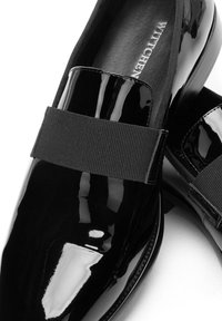 Schwarze Lacklederschuhe mit einem elastischen Band über dem Oberteil. Glänzendes Finish, runde Spitze und minimalistisches Design. Geeignet für formelle Anlässe.