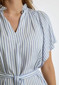 Blau-weiße gestreifte Bluse mit kurzen Rüschensäumen, V-Ausschnitt und einem passenden gebundenen Gürtel, der metallische Fadenakzente aufweist.