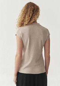 Beige színű, rövid ujjú polo póló, puha tapintással és klasszikus gallérral, egyenes aljú és minimalista dizájnnal.