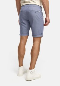 Blaue Baumwollmischung-Shorts mit umgeschlagenen Säumen, ausgestattet mit Gesäßtaschen und einem Reißverschluss. Tragen mit weißen High-Top-Sneakern.
