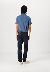 Tummansiniset slim fit -farkut, joissa on takataskut ja vyötärönauha. Vaaleansininen lyhythihainen polo-paita; kermaisen väriset tennarit.