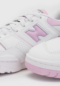 Zapatillas deportivas blancas con acentos en rosa, textura perforada, cordones y un prominente logo "N" gris. Suela de goma con acabado texturizado.