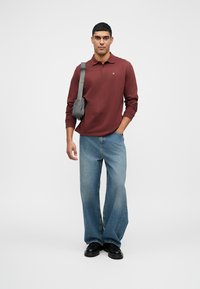 Marlitt langermet polo skjorte, lyseblå vide jeans, svarte sko og en liten svart skulderveske. Enkelt design med livlige farger.