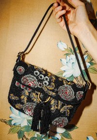 Borsa nera con perline e ricamo floreale in rosso, grigio e oro; presenta un dettaglio hardware circolare in oro e un nappa nera.