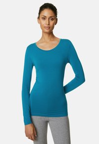 Teal långärmad topp i mjukt tyg, med rundad halsringning och figurnära silhuett, matchad med grå leggings.