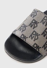 Πλατφόρμα σανδάλι με υφή, μπεζ επάνω μέρος που διαθέτει επαναλαμβανόμενο μοτίβο μαύρου λογότυπου. Μαύρη καουτσούκ σόλα με λείο φινίρισμα.