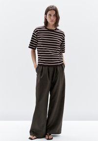 Braun-weiß gestreiftes T-Shirt mit kurzen Ärmeln, kombiniert mit lockeren, weit geschnittenen, dunklen Hosen und schwarzen Sandalen. Glattes Material mit bequemer Passform.