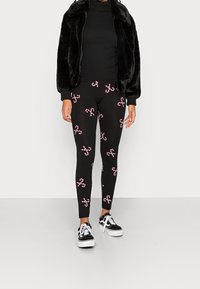Leggings noirs avec un motif de canne en sucre en rouge et blanc, associés à une veste en fausse fourrure noire et des baskets noires.