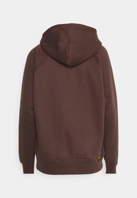 Sweat à capuche marron à manches longues avec une grande capuche, des poignets côtelés, et une petite étiquette noire et jaune près de l'ourlet inférieur à l'arrière.