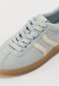 Baskets en daim bleu clair avec des accents beiges, dotées de lacets plats, d'une surface texturée et d'une semelle en caoutchouc. Étiquette bleue sur la languette.