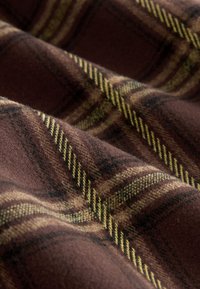 Tessuto a quadri marrone con accenti gialli e neri, caratterizzato da una texture morbida e da un motivo intrecciato di linee e quadrati che si intersecano.