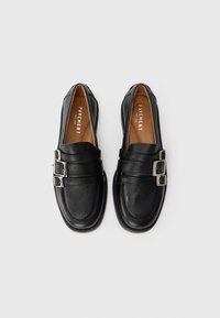 Crne kožne loafers c textured završetkom, s dva srebrna kopčanja i zaobljenim prstom. Unutrašnjost ima smeđi oblog.