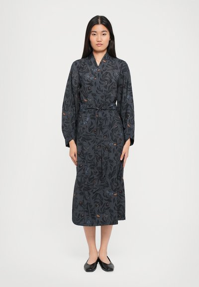 Robe florale sombre à manches longues, dotée d'une taille ceinturée et d'une coupe symétrique. Le tissu présente des motifs de feuilles et de papillons dans diverses couleurs.