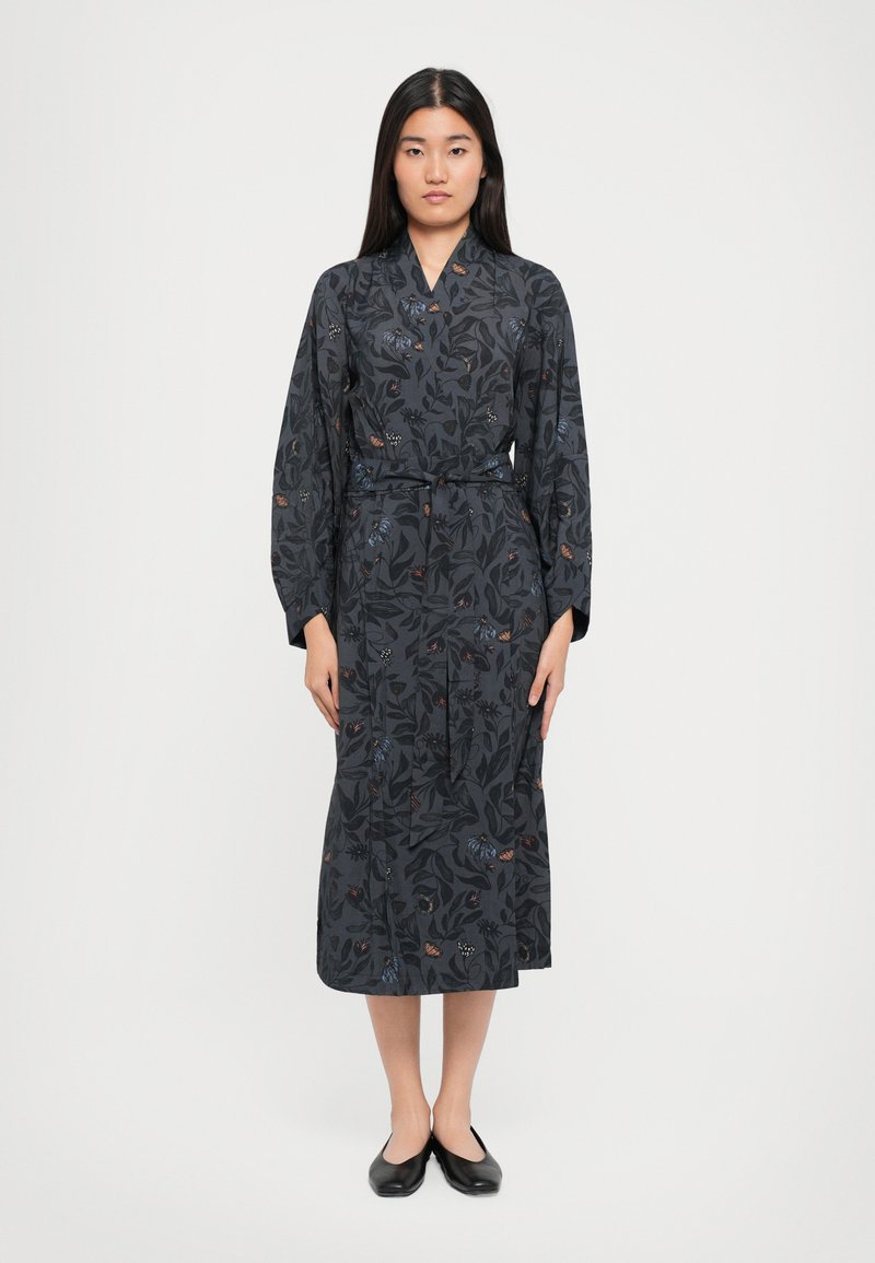 Dark floral dress with long sleeves, featuring a belted waist and a symmetrical cut. Fabric shows leaf and butterfly patterns in various colors.