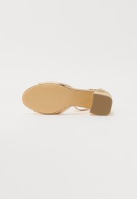 Gouden sandalen met een ronde teen, gestructureerde zool en een brede blokhak. Voorzien van een dunne enkelband en een metallic afwerking.