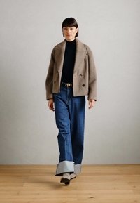 Sacou din lână maro cu două rânduri de nasturi, purtat peste un top negru, asortat cu blugi din denim albastru cu picioare largi, având un tiv contrastant.