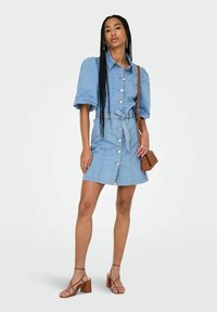 Denim shirtimekko puff-hihalla, vaaleansinisessä värissä, napitettava etuosa, vyötärössä solmittava vyö ja taskuyksityiskohta. Yhdistetty ruskeisiin paksupohjaisiin sandaaleihin.