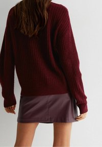 Burgundowy sweter z prążkowanej dzianiny z długimi rękawami, połączony z dopasowaną burgundową skórzaną mini spódnicą, ukazującą teksturę i warstwy.