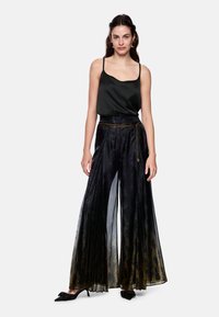 Black satin top with thin straps paired with wide, pleated sheer black pants featuring a gold and purple pattern, accented by a chain belt.