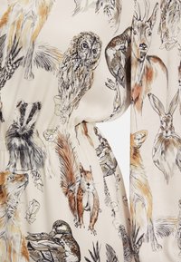 Ärmeldetail eines Stoffes mit einem hellen Hintergrund und lebhaften Tierillustrationen, darunter eine Eule, ein Fuchs und ein Dachs, mit glatter Textur.