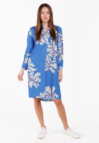 Blaues Blumenkleid mit langen Ärmeln, das große beige und rote Blättermuster aufweist. Hergestellt aus leichtem Stoff, endet es oberhalb der Knie.