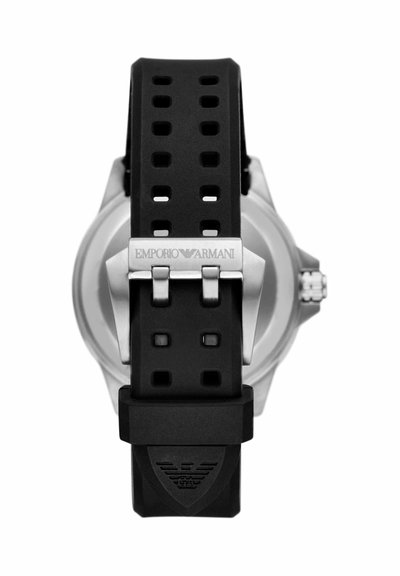 Bracelet de montre en caoutchouc noir perforé avec boucle argentée gravée « Emporio Armani » et logo embossé près de l'extrémité, attaché à un boîtier de montre argenté.