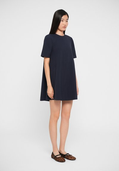 Navy A-line dress with short sleeves, made of smooth fabric. Paired with leopard print flat shoes featuring a black strap.
