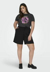 T-shirt gris foncé avec motif floral et texte, associé à un short noir à cordon. Le mannequin porte des mocassins noirs à plateforme.