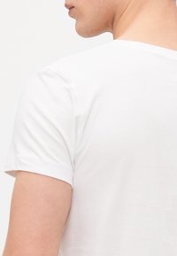 Weißes Baumwoll-T-Shirt mit kurzen Ärmeln, Rundhalsausschnitt, glatter Textur und geradem Saum. Minimalistisches Design ohne Muster oder Akzente.