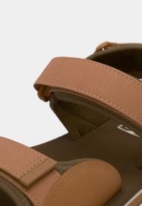 Καφέ και ανοιχτό πορτοκαλί σανδάλια με δύο ρυθμιζόμενους ιμάντες και υφή στην επάνω επιφάνεια, με επενδεδυμένο πέλμα και σχεδιασμό σόλας χωρίς ραφές.