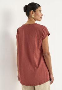 Rustfarvet kortærmet T-shirt med en afslappet pasform, rund halsudskæring og blød tekstur, vist bagfra med let materiale der draperer.