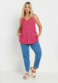 Rosa stickad ärmlös topp med diagonala ränder, utrustad med två sidofickor. Matchad med ljusblå avslappnade jeans och vita kilklackssandaler.