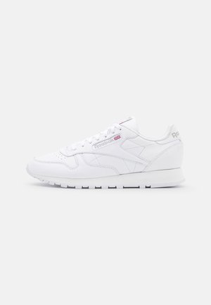 Biały, niskoprofilowy skórzany sneaker Reebok z białymi sznurowadłami, perforowanym noskiem i subtelnym logo Reebok z flagą Wielkiej Brytanii na bocznym panelu.
