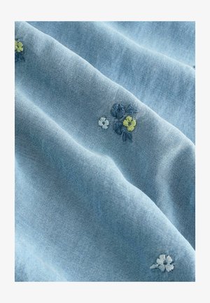 Geborduurde denimstof in lichtblauw, met bloemmotieven in geel en blauw. De textuur is glad met een subtiele glans.