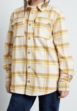 Flannelskjorte i creme og gulternet mønster med to brystlommer, knappelukning foran og rundet kant. Fremstillet af blødt, struktureret stof.