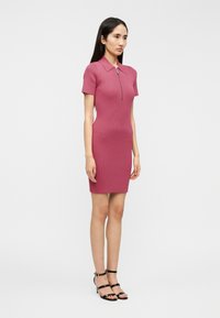 Κολλητό ροζ φόρεμα με ριμπ ύφανση, κοντά μανίκια και γιακά πόλο, με φερμουάρ στο μπροστινό μέρος και μήκος που φτάνει μέχρι το γόνατο.