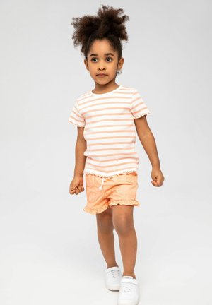 Stribet kortærmet skjorte i pink og hvid, parret med orange flæse shorts. Hvide sneakers. Glatte teksturer med afslappede designelementer.