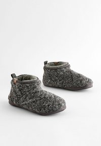 Graue gestrickte Hausschuhe mit einem strukturierten Muster, ausgestattet mit einem weichen Innenfutter, Knöchelhöhe und einem braunen Akzent an der Rückseite.
