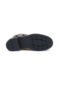 Semelle extérieure en caoutchouc noir avec un motif de grip texturé. La semelle intermédiaire est en suède gris avec un détail de bande. Design épuré et fluide.
