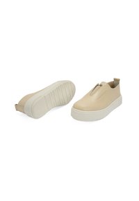 Beige instappers met een glad leren bovenwerk en elastische sluiting, met een gestructureerde witte rubberen zool en een klein lusje aan de achterkant.